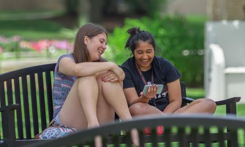 两个卡罗尔的学生坐在长凳上笑着看手机.